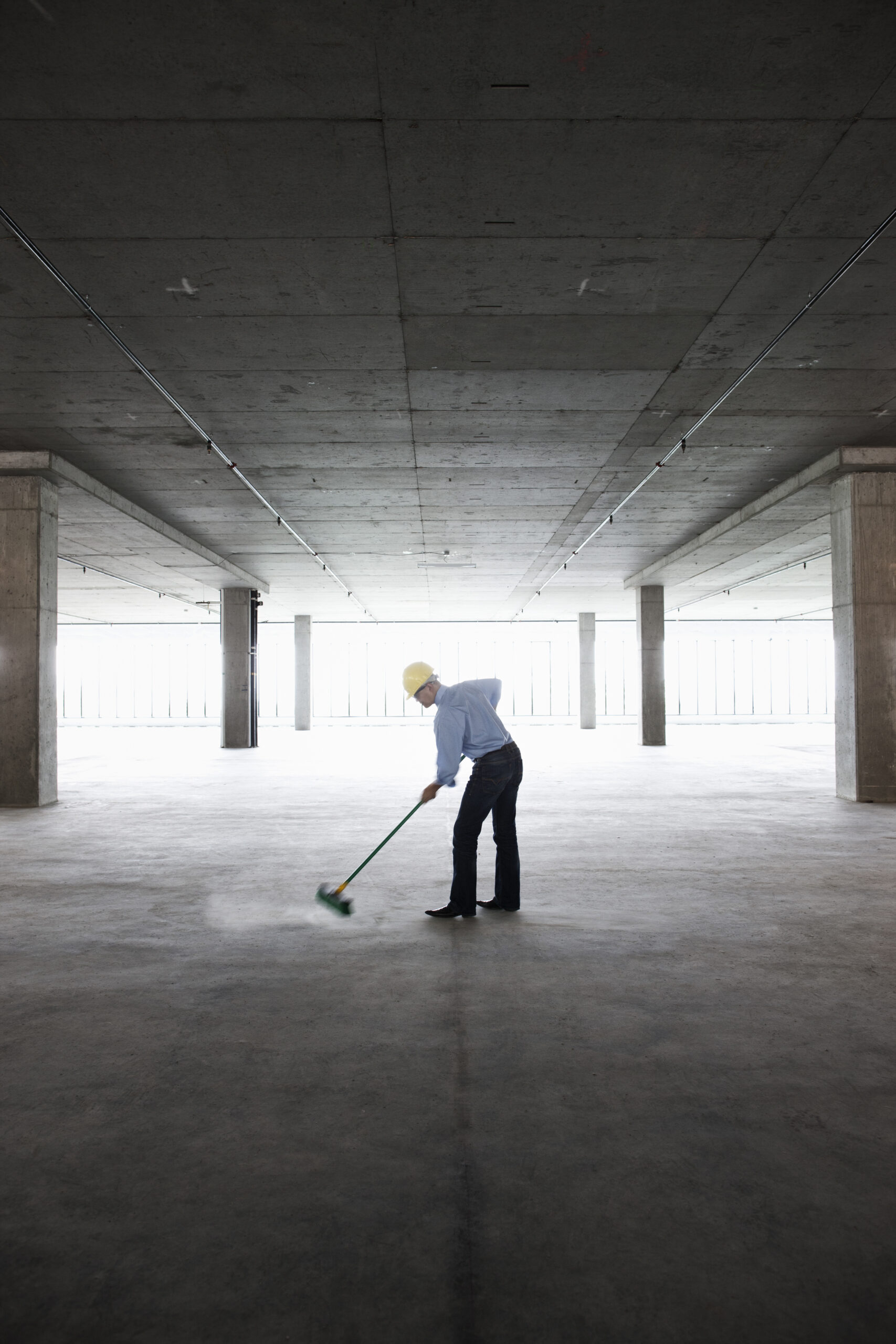 Asian businessman cleaning up with a broom in a large empty raw office space.